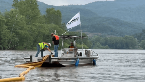 Two oil spill response technicians deploy 18 inch containment boom into the water for oil containment and recovery